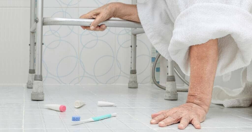 Elderly person on the bathroom floor holding onto a walker with toiletries scattered around.