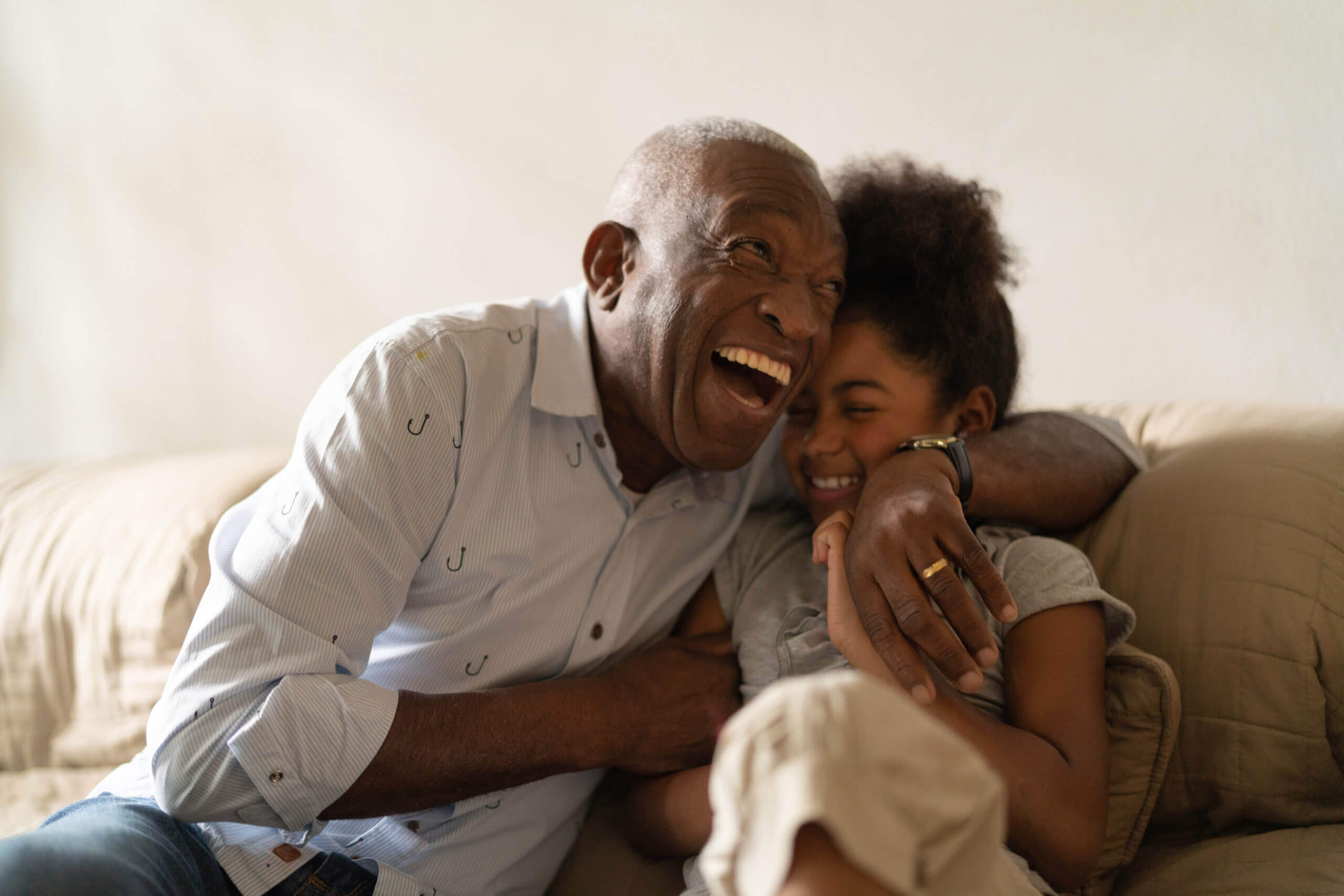 Grandfather and granddaughter sharing a joyful moment while sitting on a cozy couch.