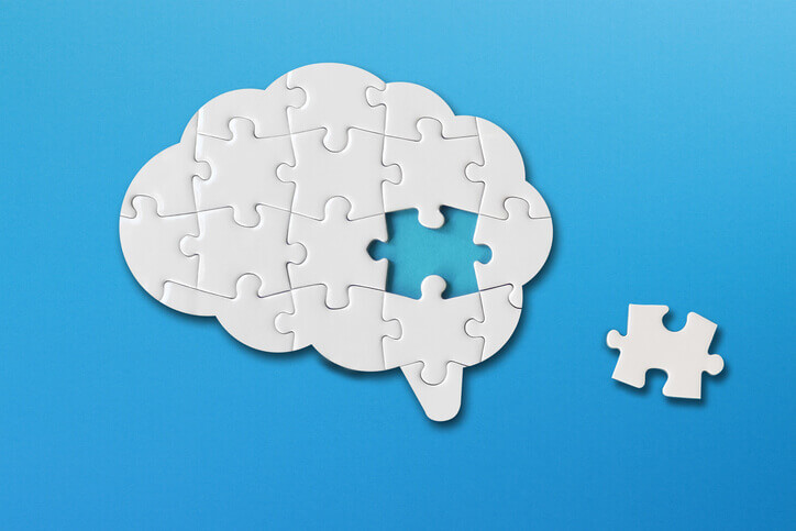 Brain-shaped jigsaw puzzle with one missing piece on a blue background.