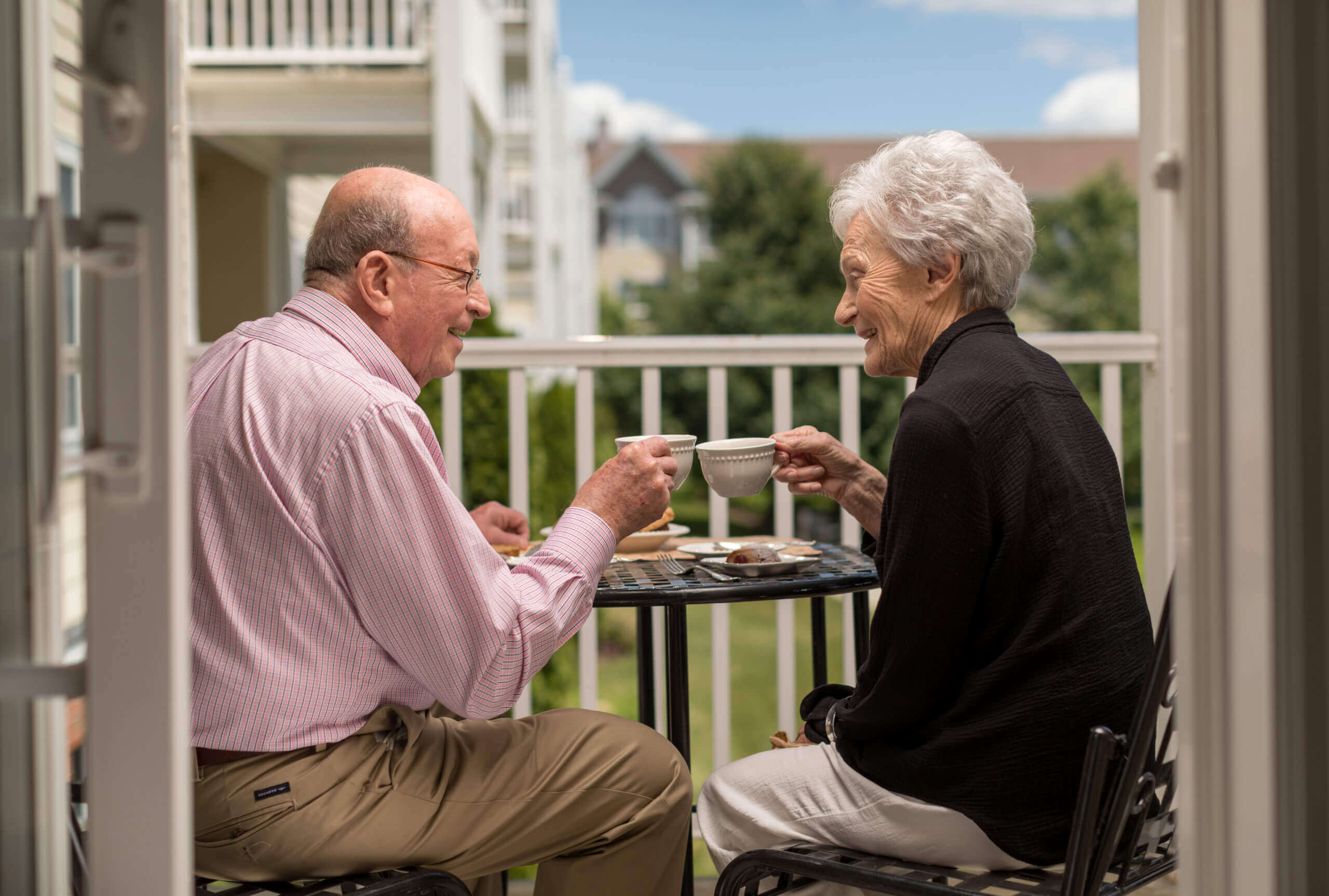 Elderly man and woman enjoying coffee on a balcony of their retirement community unit.