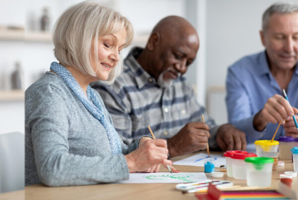 Woman smiling as she and two men paint pictures at a table