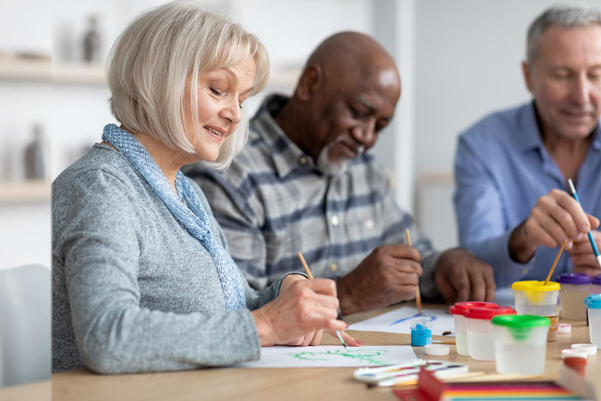 Woman smiling as she and two men paint pictures at a table