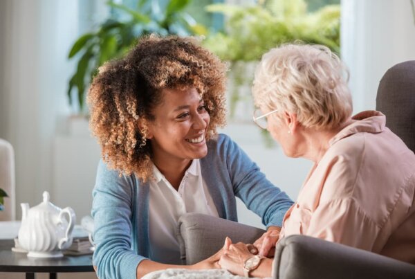 Adult woman checking in on senior woman and holding her hands
