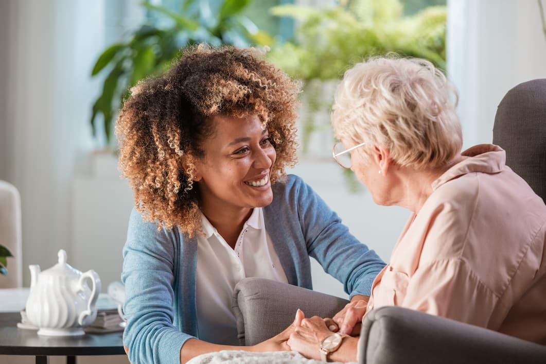 Adult woman checking in on senior woman and holding her hands