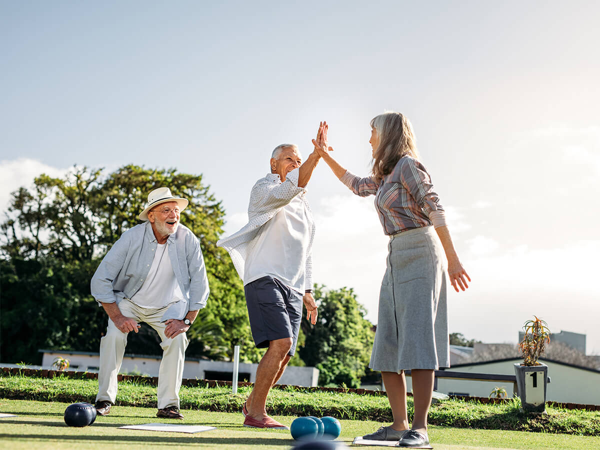 Seniors playing lawn bowls and celebrating with a high five outdoors.