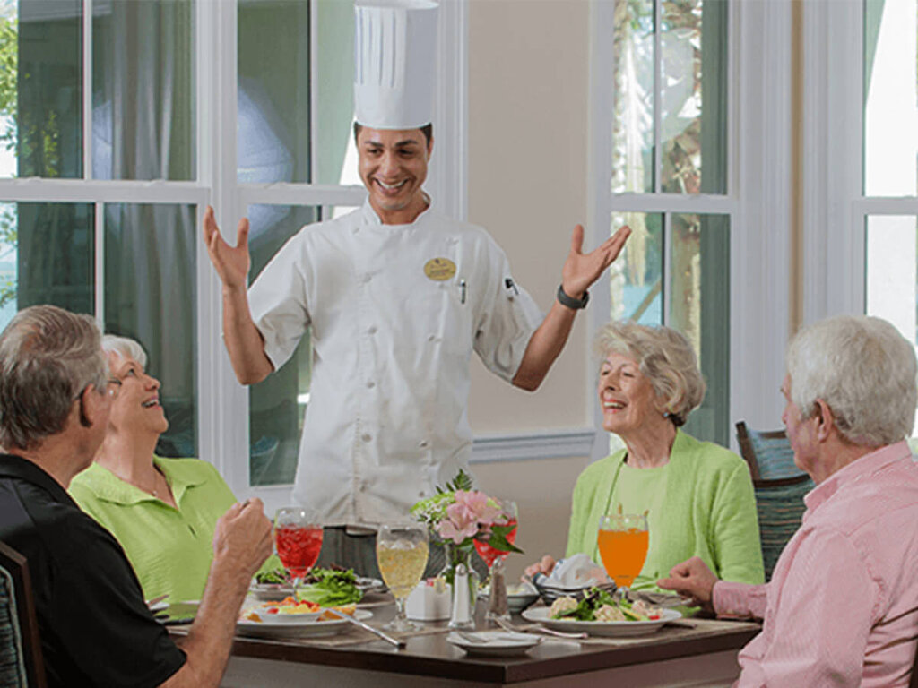 Chef engaging with seniors enjoying a meal in a vibrant dining area.