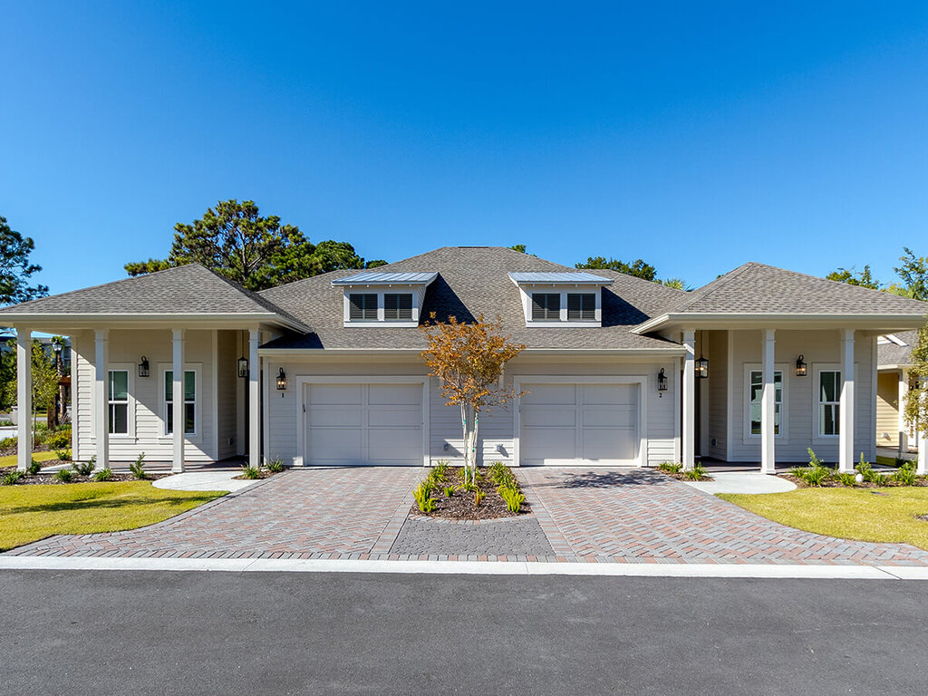 Two-unit residential building with beige siding and well-kept landscaping under blue sky.