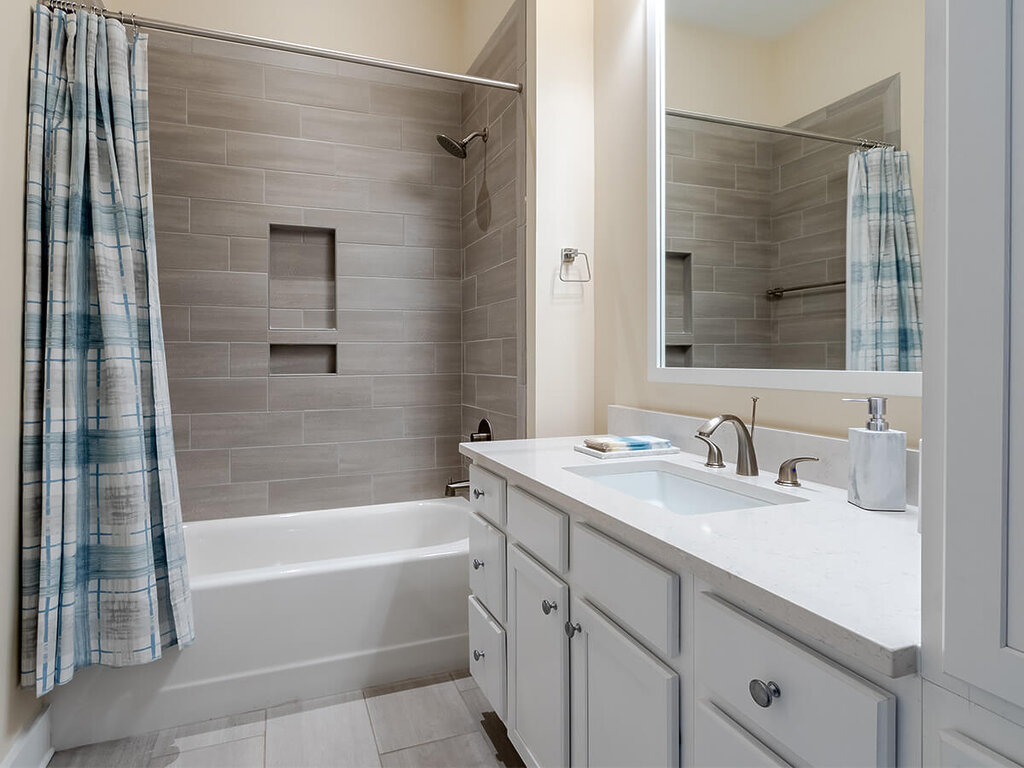 Modern bathroom with a white vanity, sink, and tiled shower area in a living unit.