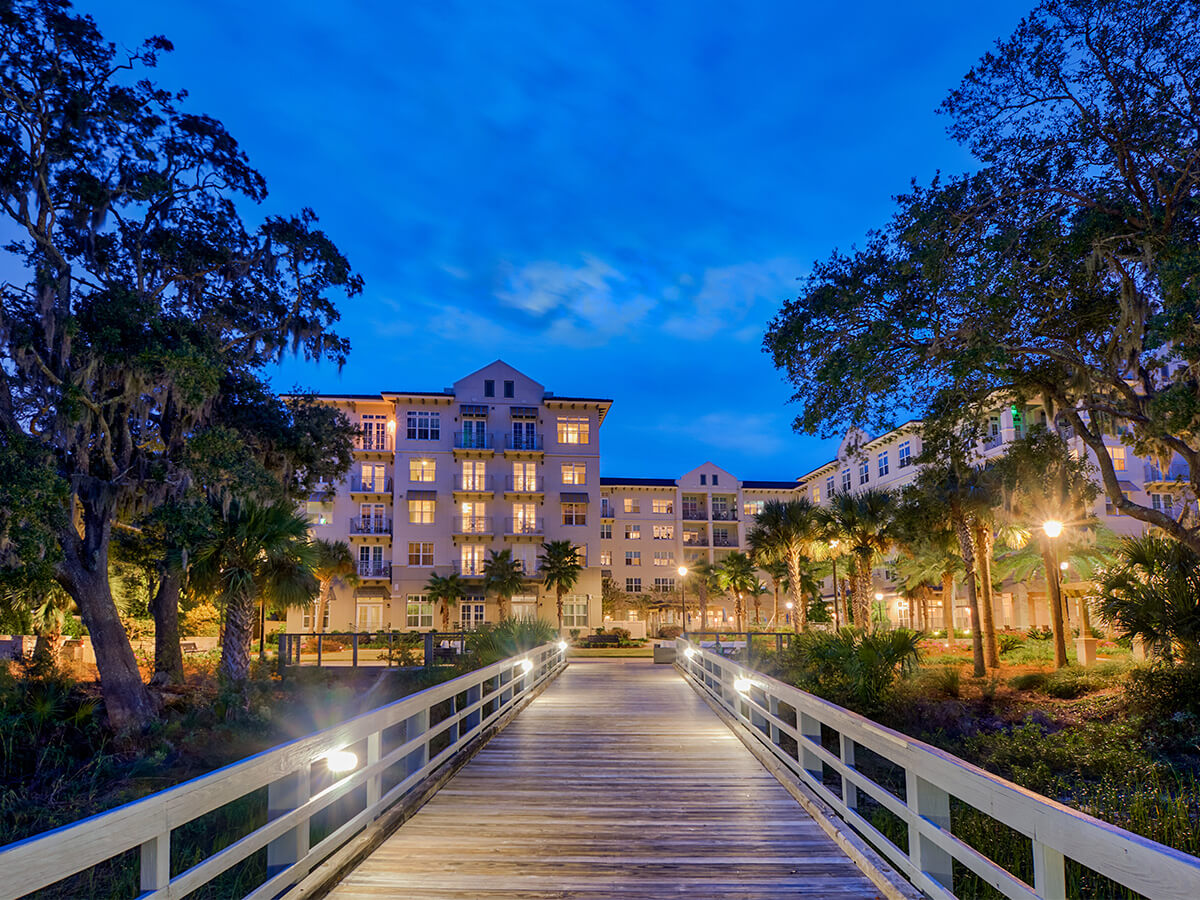 Elegant building at dusk with illuminated windows and a wooden pathway.