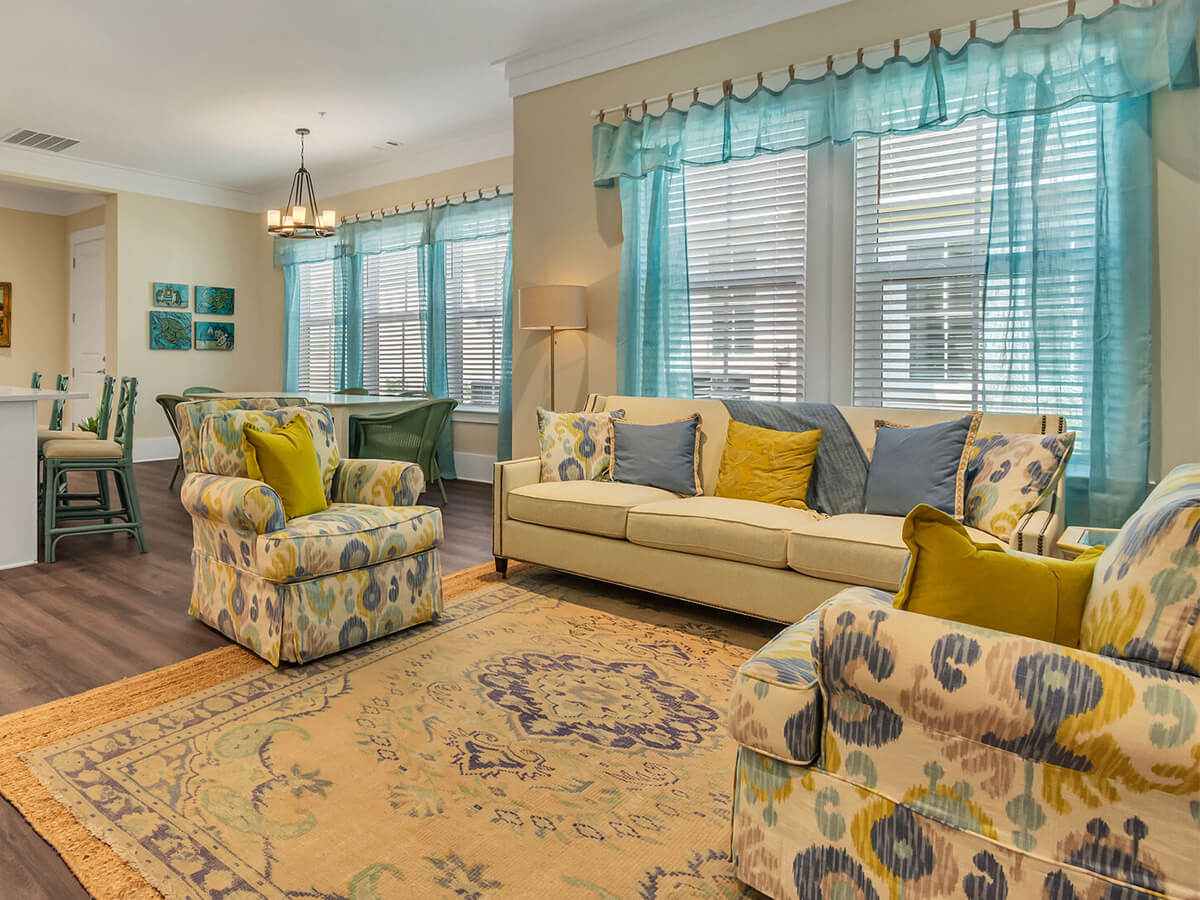 Comfortable living room with a beige sofa, patterned chairs, and blue curtains.