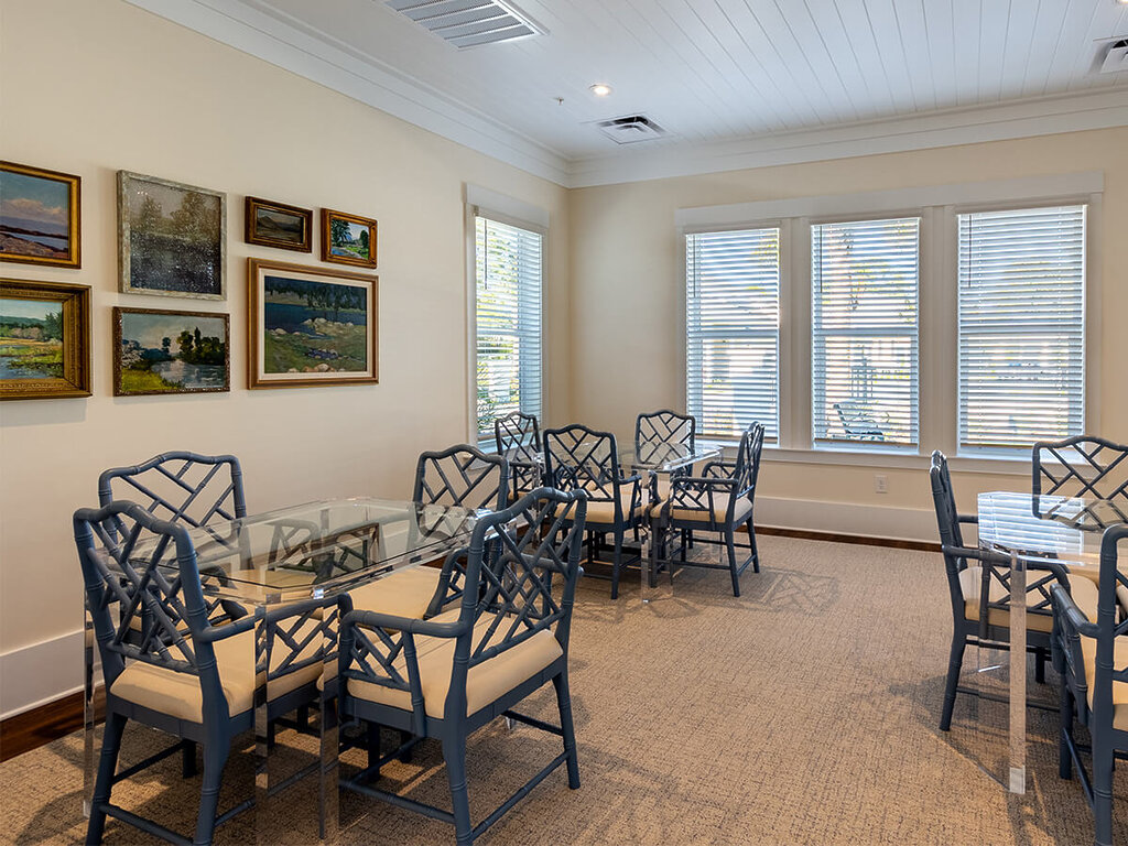 Bright dining area with blue chairs and scenic paintings on cream walls.