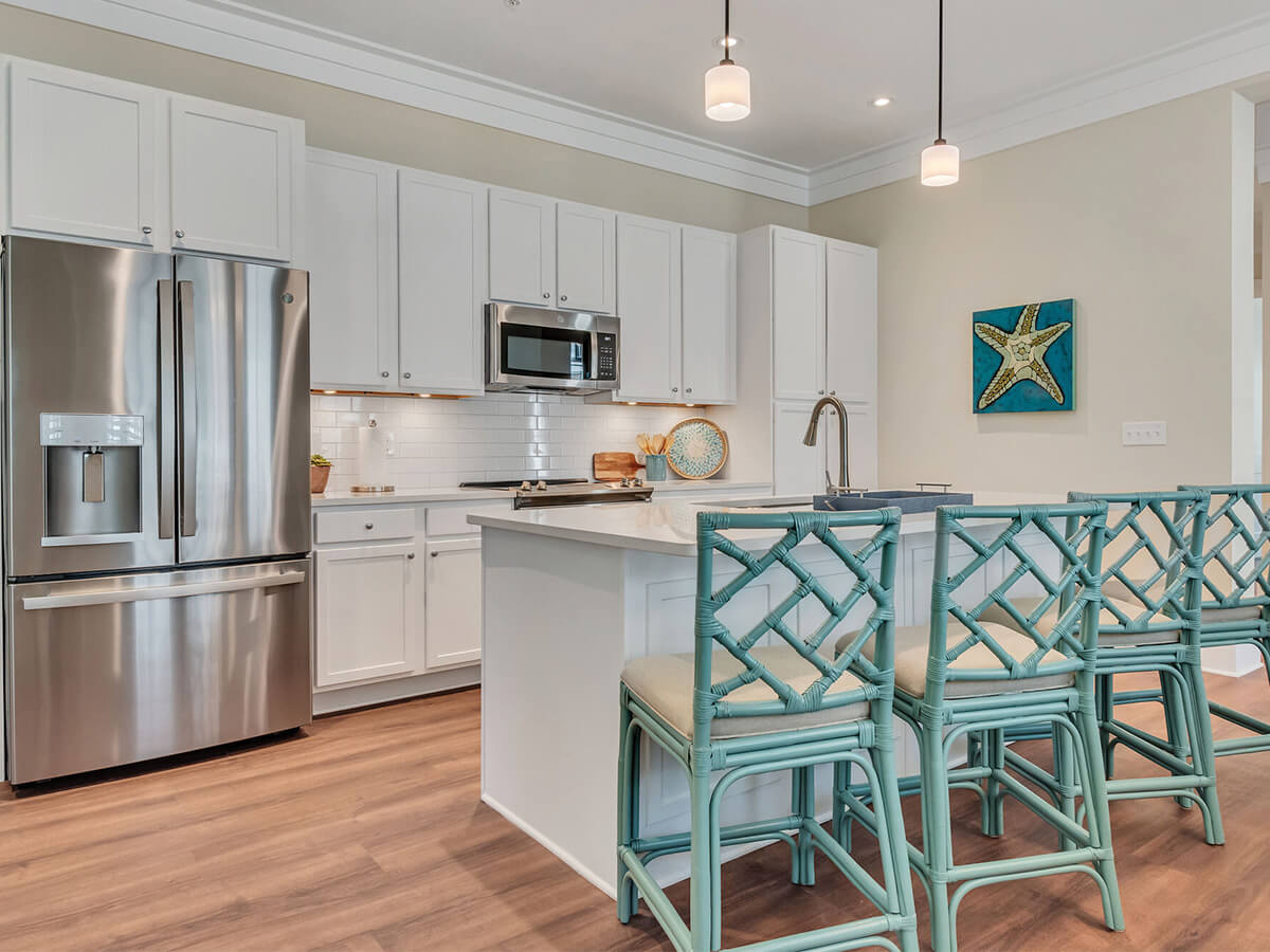 Modern kitchen with white cabinets and aqua barstools in a senior living unit.