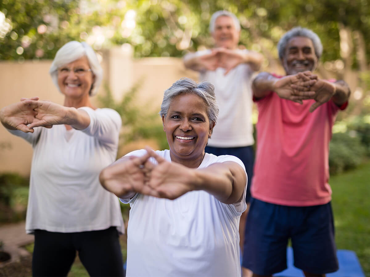 Seniors practicing outdoor exercises, smiling, in a lush garden setting.