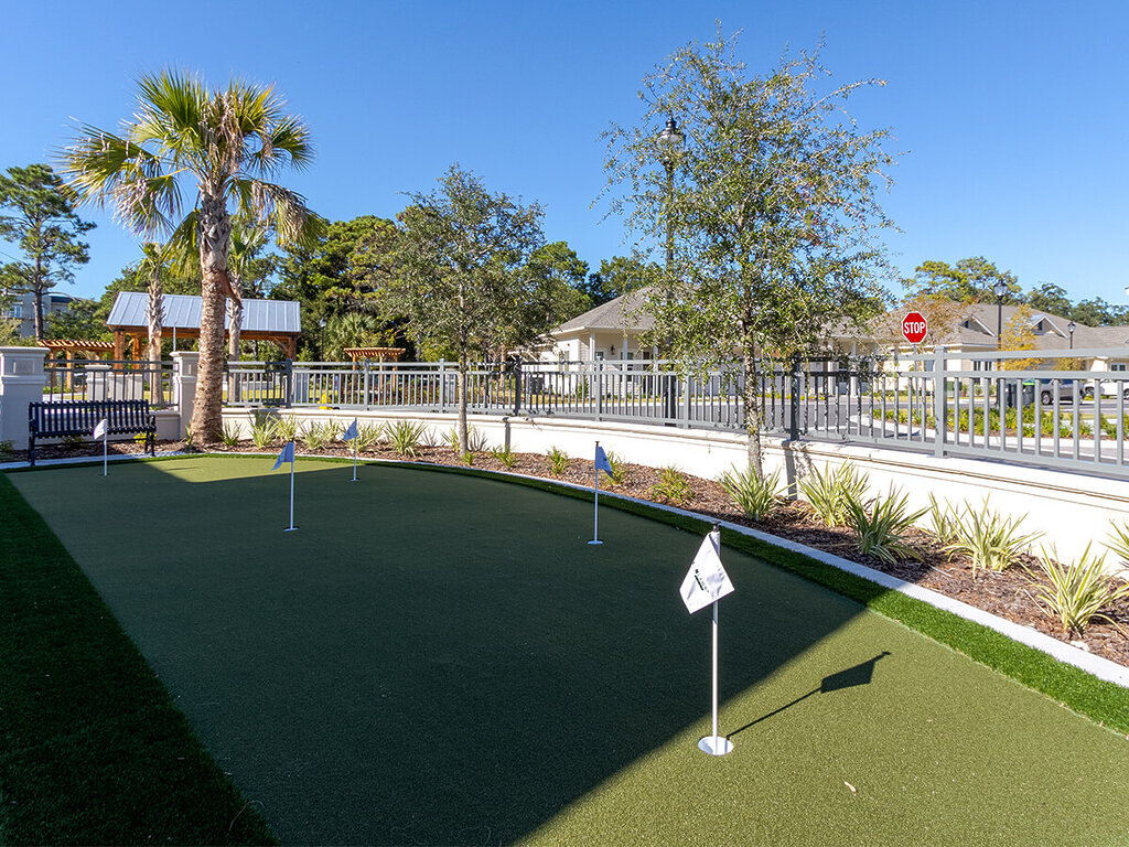 Outdoor putting green with flags, palm tree, and bench at a senior living community.