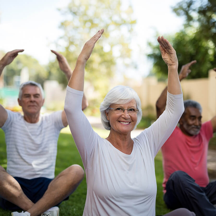 Seniors practicing outdoor yoga in a community garden, smiling and raising arms.