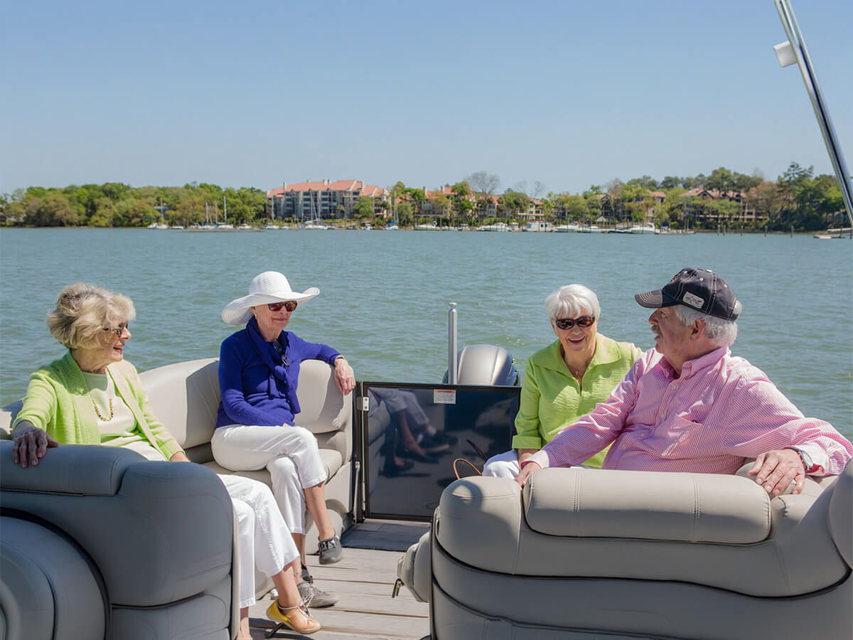 Four seniors enjoying a sunny day on a boat with scenic waterfront views.