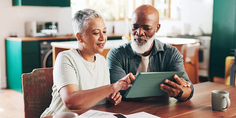 Two seniors using a tablet in a modern kitchen setting, smiling and engaged.