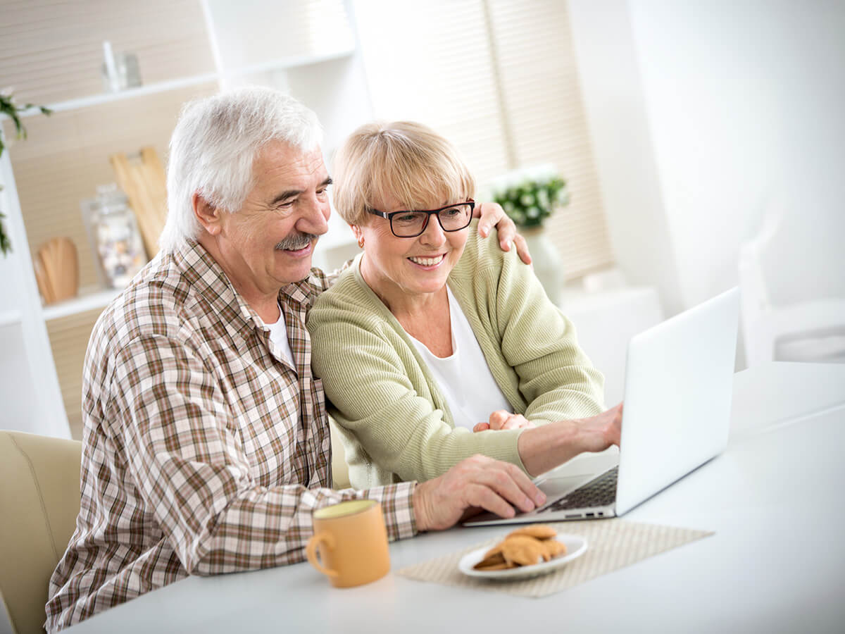 Smiling senior couple using a laptop at a table in a bright living space.