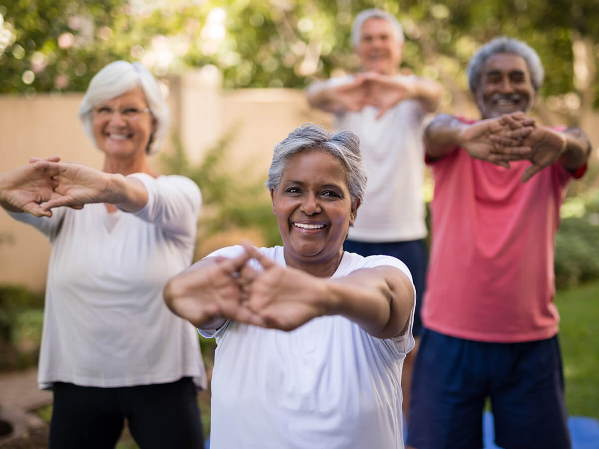 Four seniors smiling and stretching outdoors in a garden area.