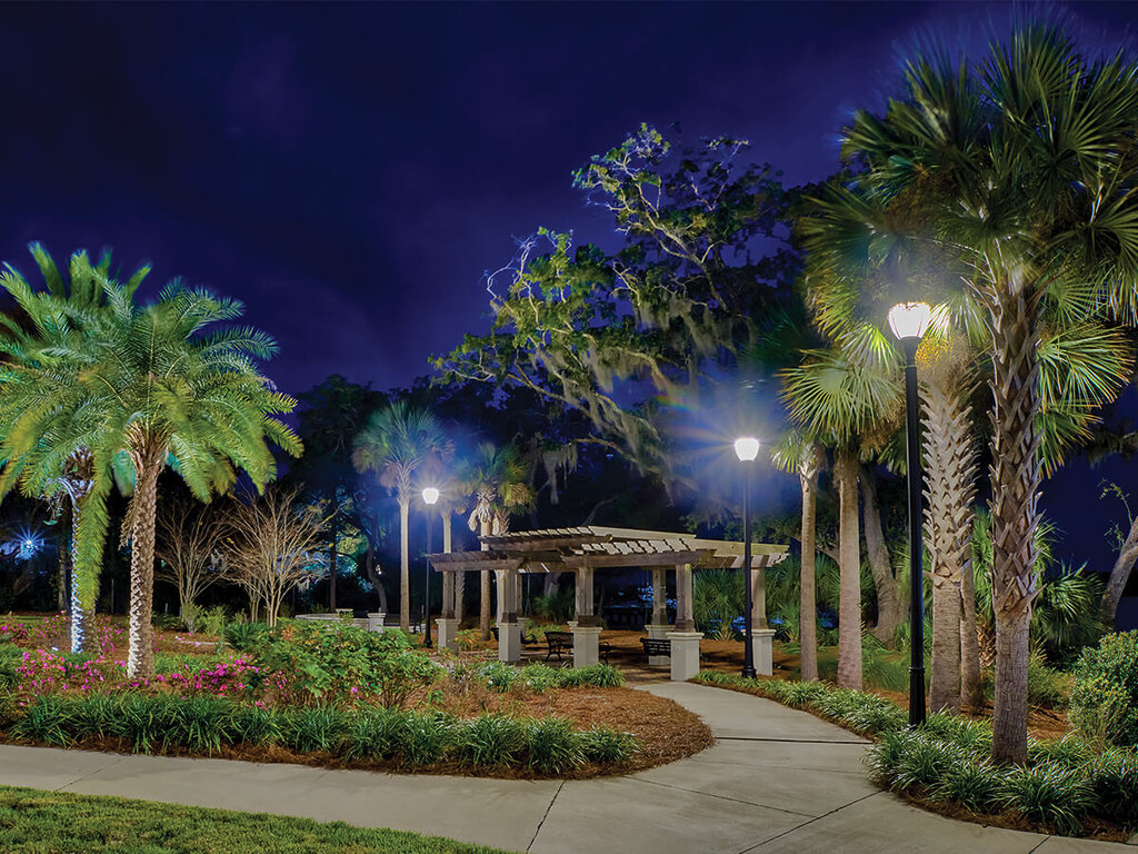 Scenic nighttime walkway with palm trees and pergola in a landscaped garden.