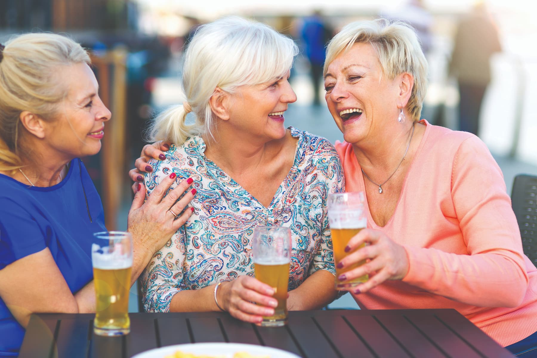 Senior women sitting around a table laughing and enjoying beers